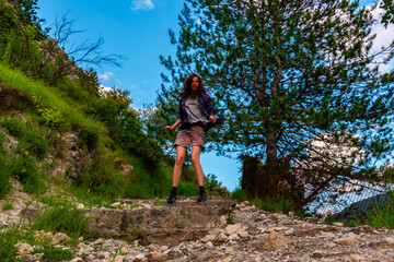 A full body shot of an energetic young Caucasian redhead woman jumping on a hiking path in the mountains under warm summer sunlight (Puget-Theniers, France)