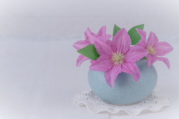 Fototapeta na wymiar Bouquet of pink clematis in a blue vase on a light background