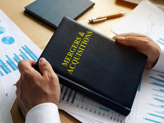 Businessman holds book about mergers and acquisitions MA.
