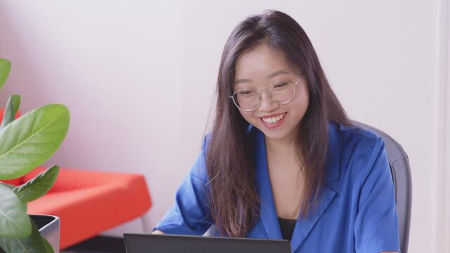 A young Asian woman is listening and smiling to a video call to relatives and friends with a laptop at home. Concept of technology, modern generation, family, connection, authenticity. - slow motion