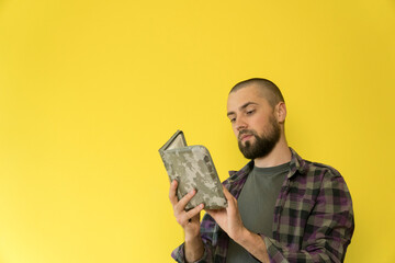 A young caucasian man with a beard on a yellow background is reading a book in a military cover. Focused an serious guy with copy space