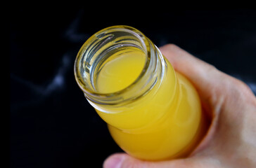 Closeup an opened bottle of orange juice in hand on black background
