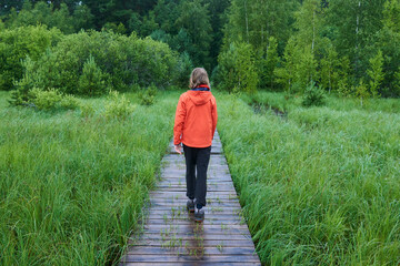 Naklejka na ściany i meble Teenager boy walking on a wooden sidewalk during a rainy day in a nature reserve