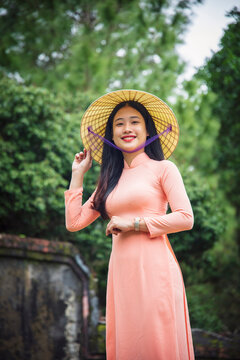 Portrait of a young Vietnamese woman in an Ao Dai dress and conical hat at a Buddhist temple, Hue, Vietnam