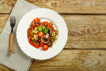 On a wooden table is a white plate of boiled mung bean with vegetables and mushrooms on a napkin and a fork. Copy space.