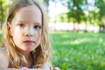 Portrait of a beautiful little girl with loose blond hair on a background of summer greenery.