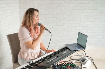 A woman records a vocal lesson using a laptop and accompanying on a keyboard while at home. The teacher sings a song into the microphone and plays the electronic piano. A blogger is recording a video.
