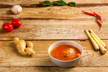 Traditional Thai Tom Yam soup in a plate next to garlic and lemograss, kaffir lime, chili and cherry. copy space