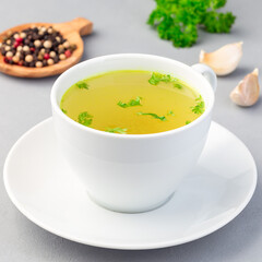 Chicken broth in white cup with chopped parsley, square format