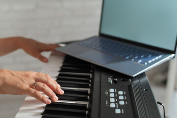 Closeup of female hands on an electronic piano. A laptop on a keyboard instrument. Online lesson....