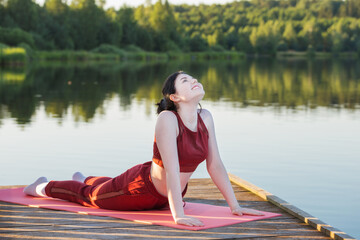 Fototapeta na wymiar girl doing yoga on wooden pier by lake in summer