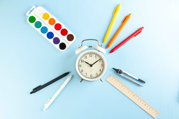 White alarm clock surrounded by colored pens and other school supplies. Art concept of the beginning of the school year