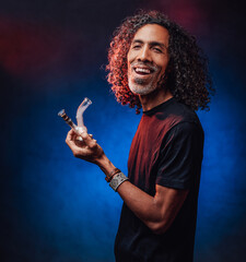 Hispanic male smoking marijuana from a bong on a dark background illuminated by blue light, get high. Cannabis legalization concept