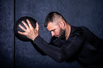 Man working out with his medicine ball on grey background. Bearded handsome young muscular sportsman is working out with a medicine ball in gym.