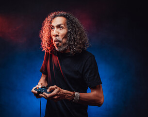 Emotional aged hispanic male with long curly hair playing video game with joystick. Hi-tech concept with vr glasses