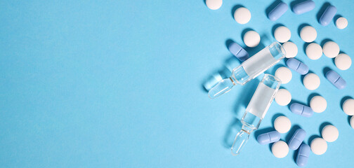 Space for text on the left side .Transparent ampoules with liquid medicine are on blue background around tablets which form polka dots pattern.