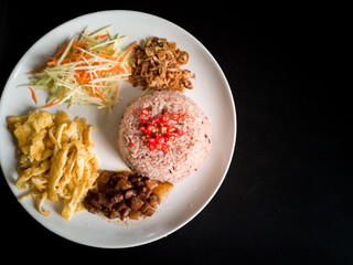 Thai food, rice mixed with shrimp paste on a white plate on a black table