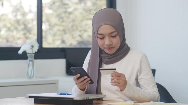 Asia muslim lady using phone, credit card buy and purchase e-commerce internet in office. Stay at home, online shopping, self isolation, social distancing, quarantine for coronavirus prevention.