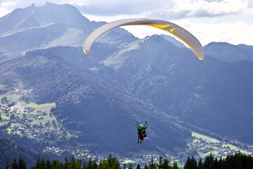 Paragliding among the mountains on sunny summer day. Paraglider flight against beautiful mountains landscape and bright sky. Parachuting in the mountains. Human flying high in the sky. Freedom concept