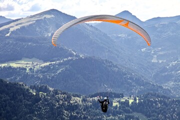 Paragliding among the mountains on sunny summer day. Paraglider flight against beautiful mountains landscape and bright sky. Parachuting in the mountains. Human flying high in the sky. Freedom concept