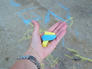 one woman's hand holds crayons, drawing with chalk on the asphalt by young children. close-up, selective focus