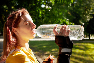sport woman drinking bottle water over public park background. sun light. girl dressed yellow shirt...