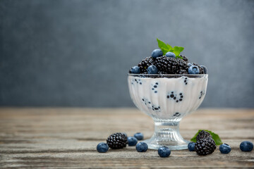 Fototapeta na wymiar Milk dessert with ripe blackberries and blueberries in a glass vase on a wooden background.