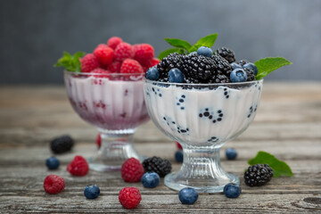 Dessert of cream, raspberries, blueberries and blackberries in glass vases on a wooden background.