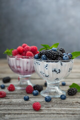Dessert of cream, raspberries, blueberries and blackberries in glass vases on a wooden background.