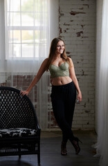 Obraz premium Stunning young woman wearing a green bustier top and black pants stands next to a black wicker chair - studio fashion