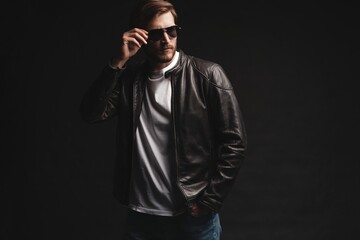 Fototapeta premium Fashion man, Handsome serious beauty male model portrait wear sunglasses and leather jacket, young guy over black background