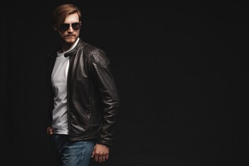 Fototapeta premium Fashion man, Handsome serious beauty male model portrait wear sunglasses and leather jacket, young guy over black background