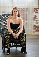 Beautiful young woman in camoflauge pants and strapless top poses with chair in studio