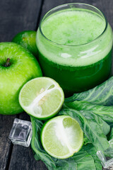 Green apple smoothie in glass and kale leaves on wooden table