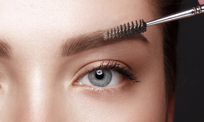 Close-up of female eyes with an eyebrow brush. Eye makeup cosmetics.
