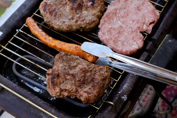 Traditional serbian barbecue (rostilj)  homemade sausages and burgers. Preparing a barbecue on a grill, Barbecue tong,outdoor roasting meat. Traditional Balkan cuisine, close up