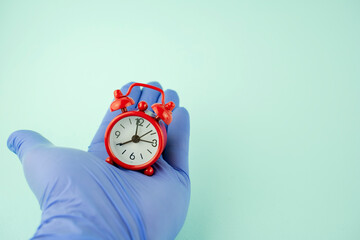 hand in a rubber glove with a red alarm clock, the concept of cleaning time and cleanliness