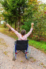 Young happy handicap woman in wheelchair on road in hospital park enjoying freedom. Paralyzed girl in invalid chair for disabled people outdoor in nature. Rehabilitation concept.
