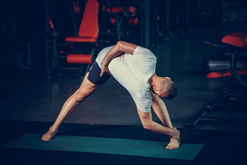 Sporty young man practicing yoga, doing stretching exercise, extended triangle pose, utthita trikonasana asana for flexible spine and relieving stress at gym.