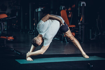 Sporty young man practicing yoga, doing stretching exercise, extended triangle pose, utthita trikonasana asana for flexible spine and relieving stress at gym.