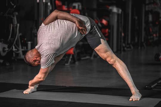 Sporty bearded young man practicing yoga, doing stretching exercise, extended triangle pose, utthita trikonasana asana for flexible spine and relieving stress at gym.