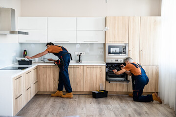 Repair. Two handymen, workers in uniform fixing, installing furniture and equipment in the kitchen,...