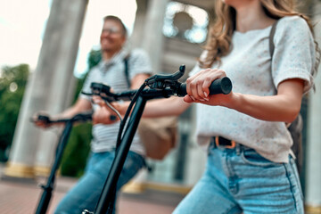 Obraz premium Cropped image of A charming girl and an attractive guy on electric scooters. A couple of students on scooters near the campus.