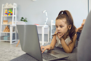 Distance education. Little girl using laptop for online class at home. Cute kid watching educational video on web