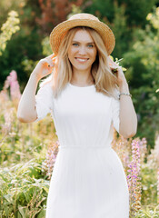 Magnificent blonde in a straw hat walks through a lupine field.