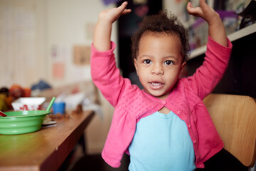 Mixed race baby girl with arms raised at table