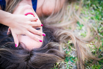 Close up portrait from above of a beautiful cheerful caucasian girl laughing a lot and having a lot of fun lay down on the grass in outdoor leisure activity - happiness and joyful people concept