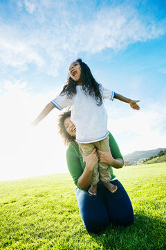 Mixed race mother holding daughter pretending to be airplane