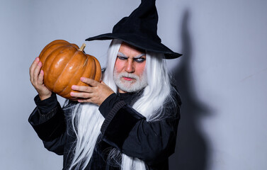 Mature man magician in witch hat. Evil wizard hold orange pumpkin. Traditional food. Fantasy horror...