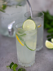 Lemonade in a glass with a slice of lime. Summer set with lemonade. Refreshing summer lemonade with lime lemon and mint in the background. Spiral and lime wedges